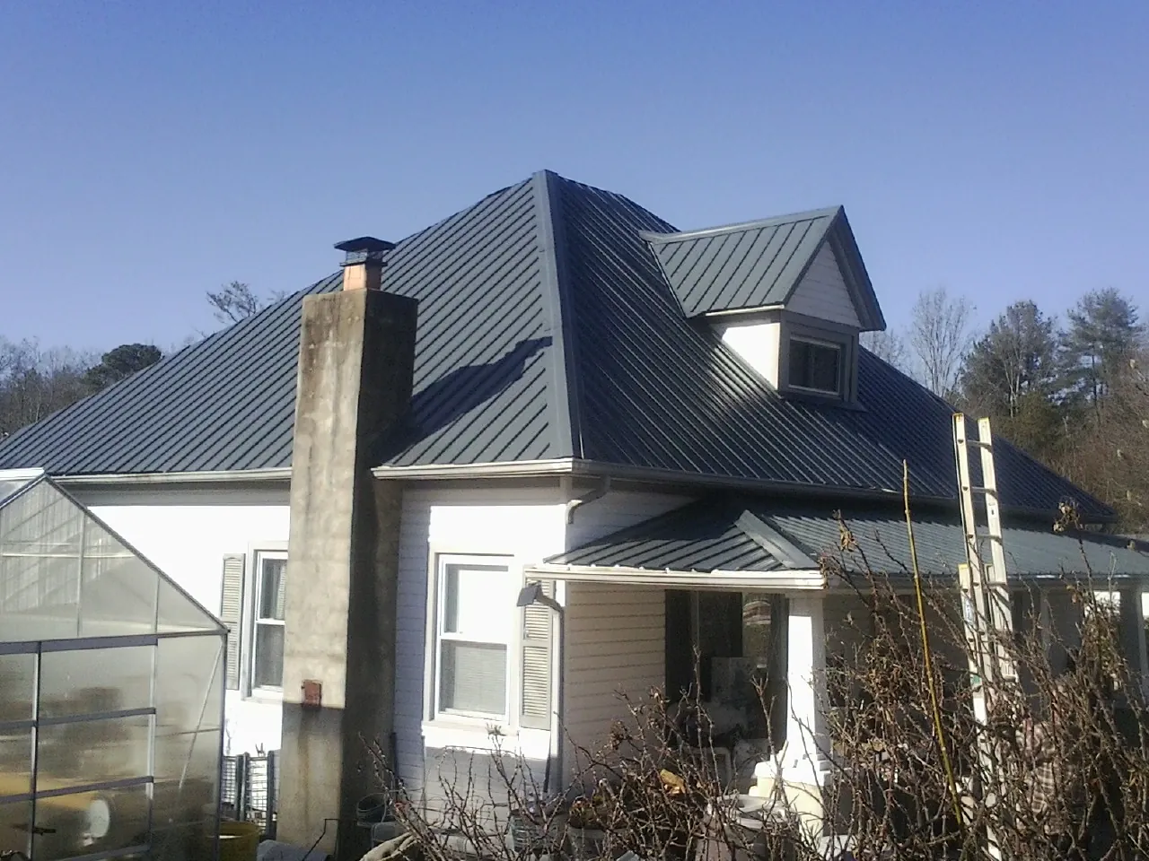 Dark blue standing seam metal roof on a white farmhouse with dormer — Slate & Tile Roof Repair by Roofing Brothers in Mc Gaheysville