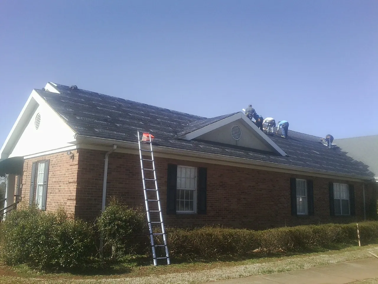 Crew tearing shingles off a brick ranch roof with a ladder set — Emergency Roof Repair work by our crew in Mc Gaheysville