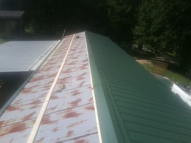 Old rusted panels beside newly installed green metal roofing — Wind Damage Roof Repair by Roofing Brothers in Mc Gaheysville