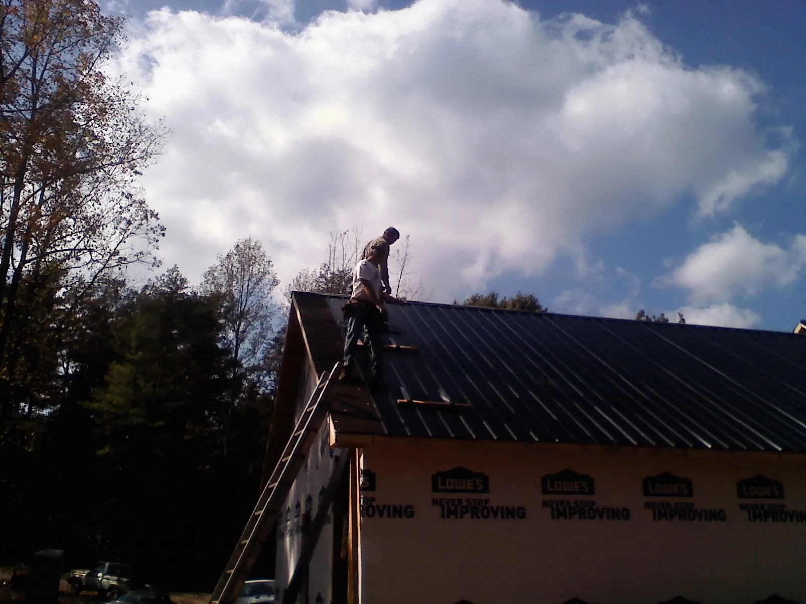 Roofer fastening dark metal panels high against a cloudy sky, from a Roof Inspection job in Mc Gaheysville