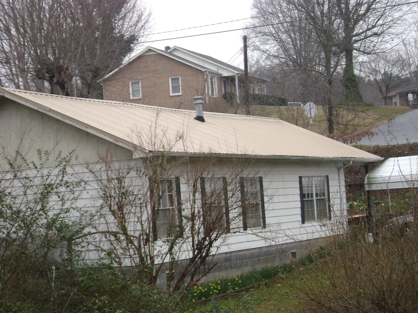 Tan metal roof on a white sided house set into a hillside in Mc Gaheysville